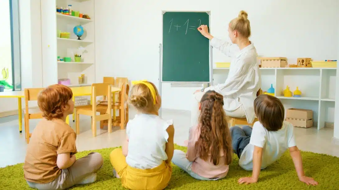 Enseignante assise au sol face à un groupe d’enfants attentifs dans une salle de classe colorée, évoquant une future carrière en éducation