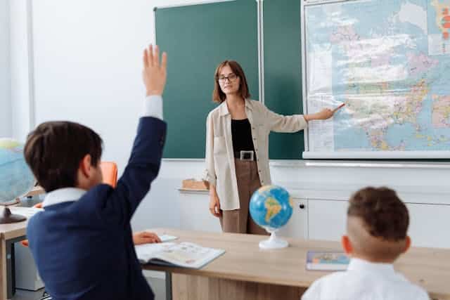 Institutrice pointant une carte en classe devant des élèves, illustrant les compétences pédagogiques développées aux USA